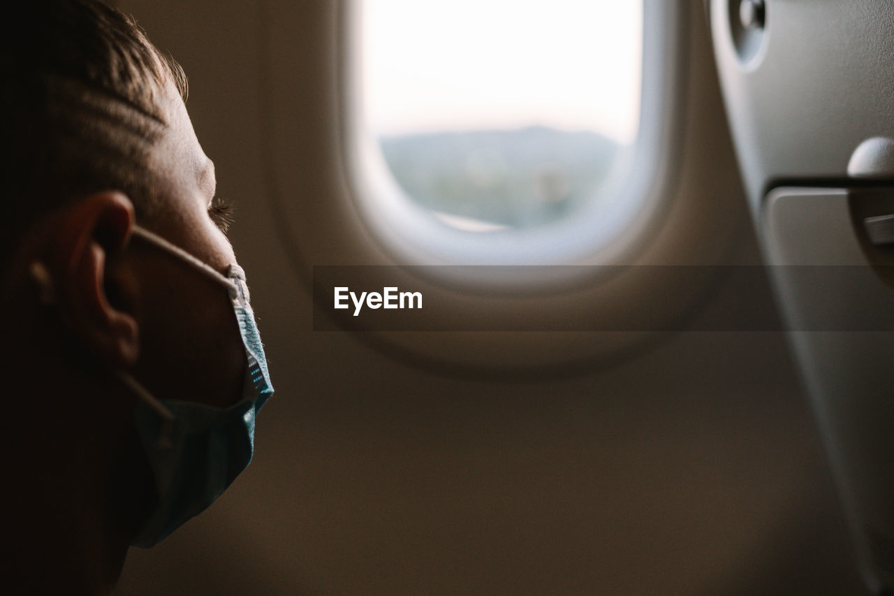 Kid in face mask admiring view behind plane window while travelling during epidemic