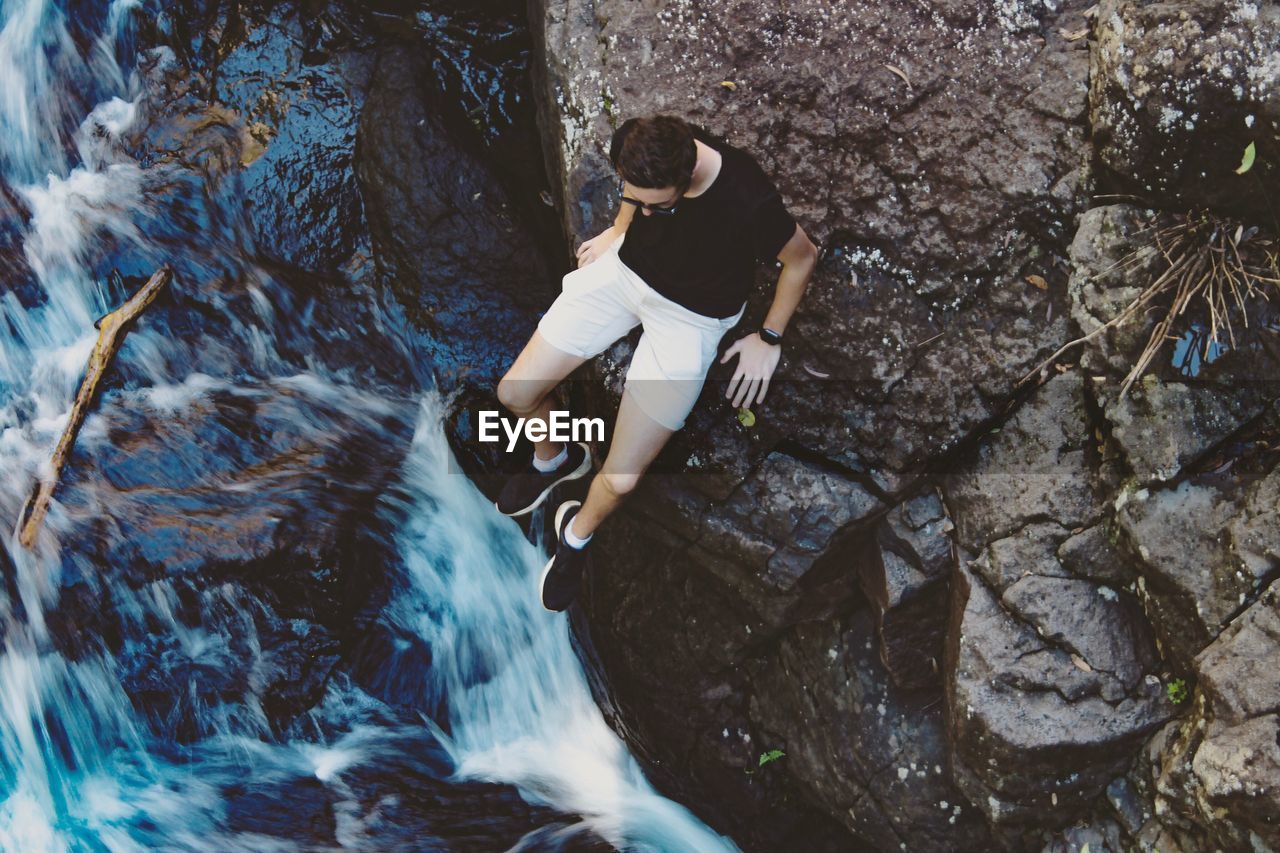 High angle view of man sitting on rock by river