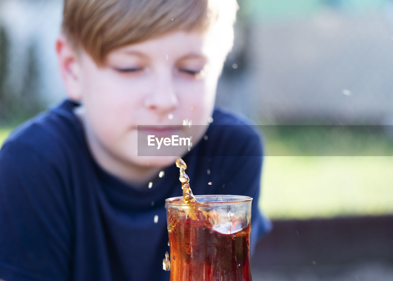 Caucasian boy watches a splash of tea in a cup from a falling piece of sugar