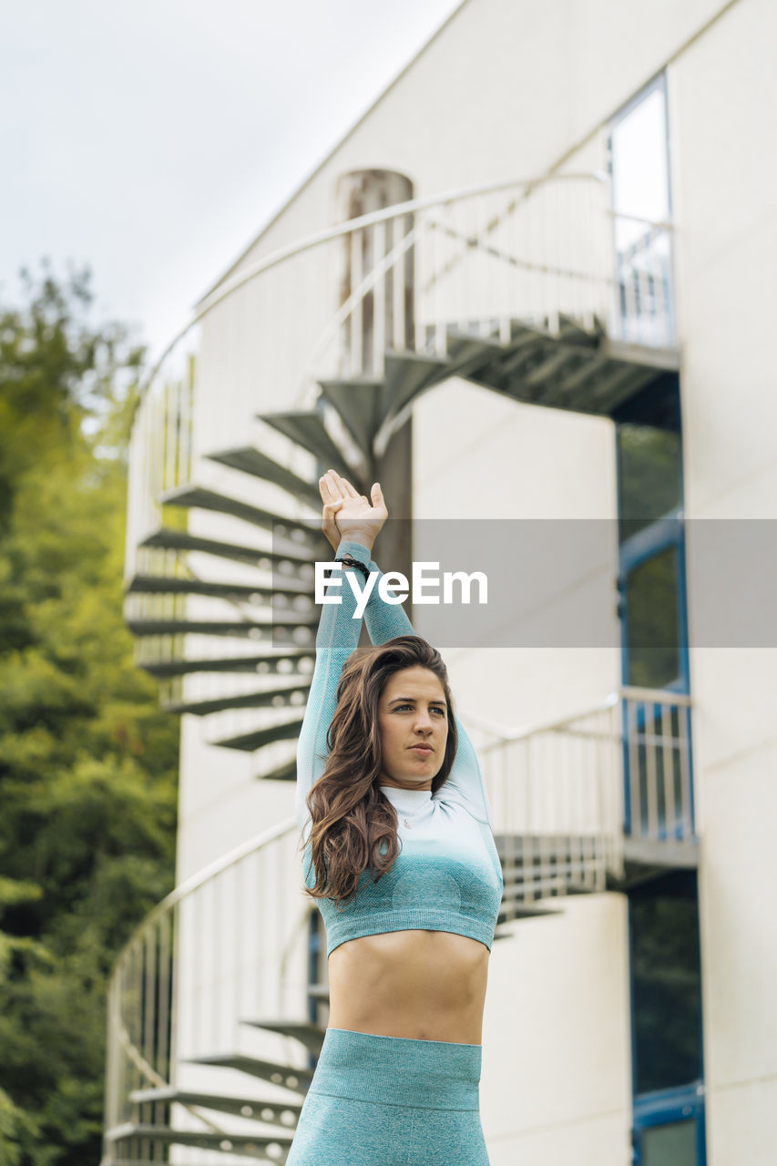 Confident sportswoman with hands raised against steps