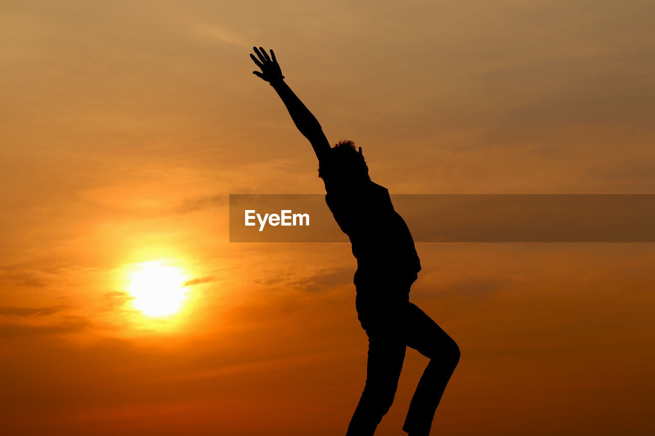 Low angle view of man with arms raised standing against orange sky