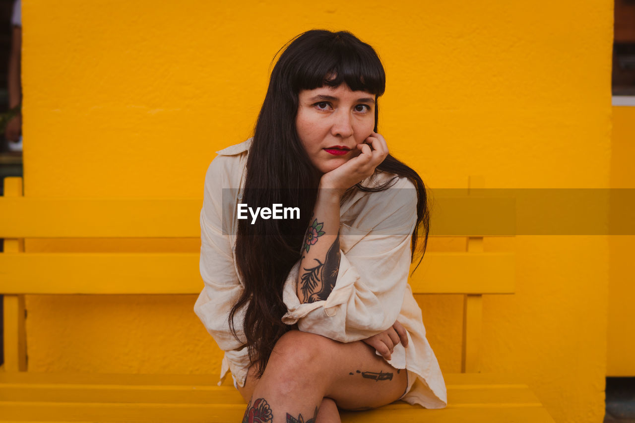 Young woman sitting against yellow wall