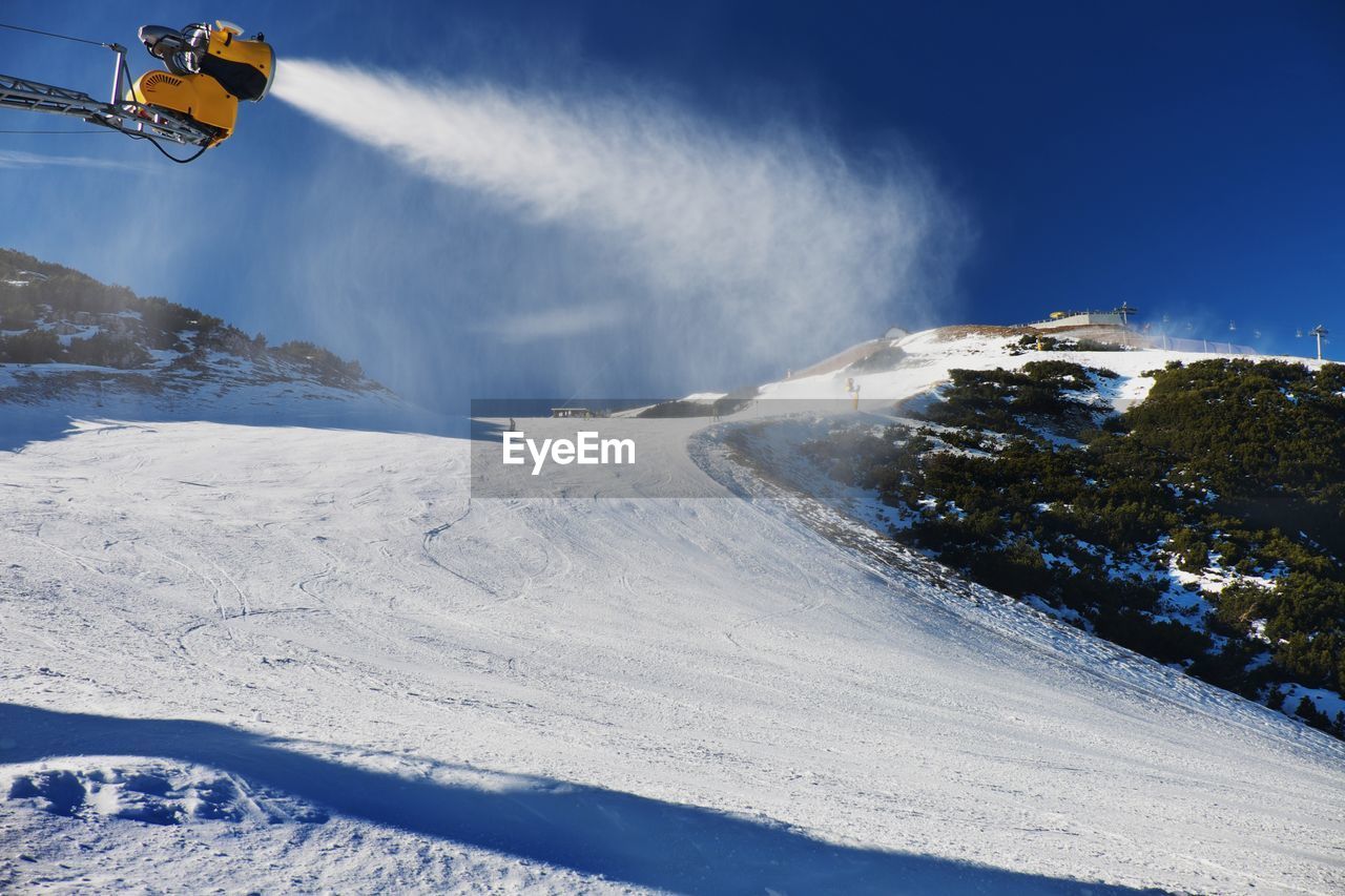 Skier near a snow cannon making fresch snow. mountain ski resort and winter calm mountain landscape.