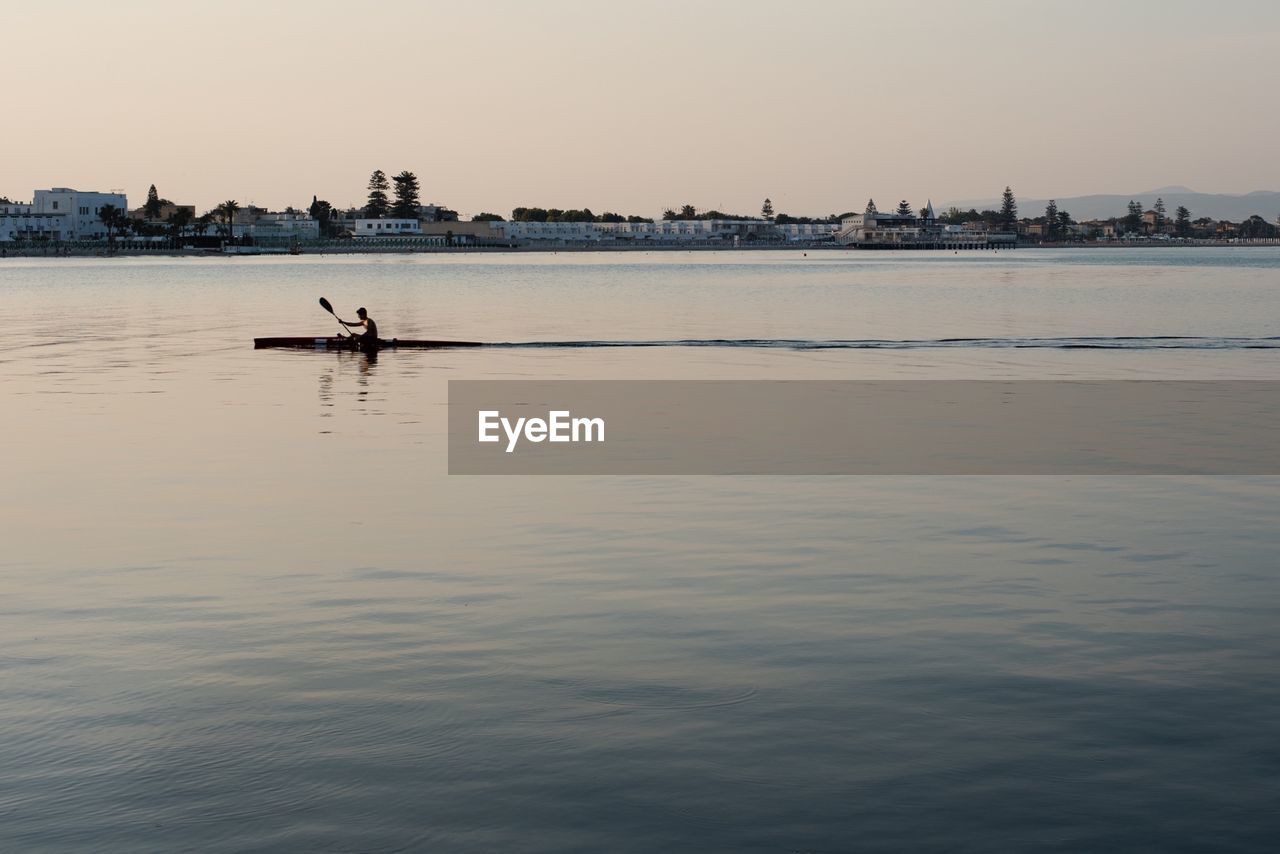 Man rowing boat on river against city and sky