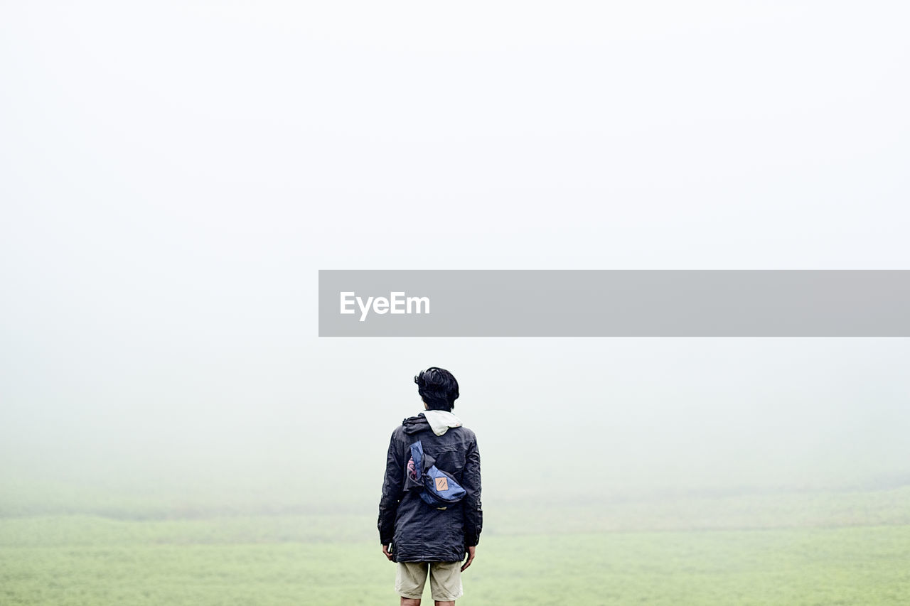 Rear view of man standing on field against sky in foggy weather