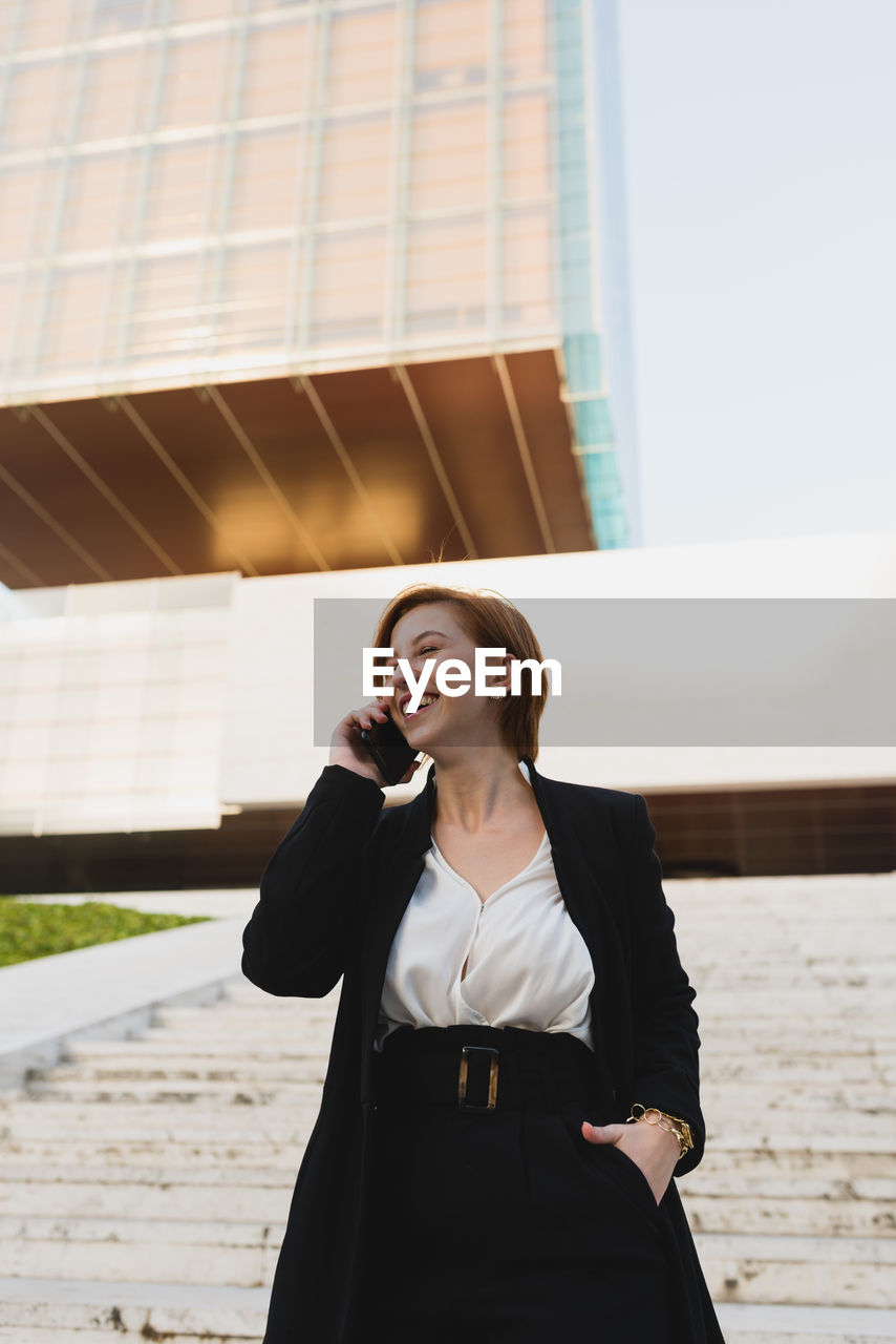 From below content female manager in elegant suit walking down the stairs in city and discussing work issues on cellphone while looking away