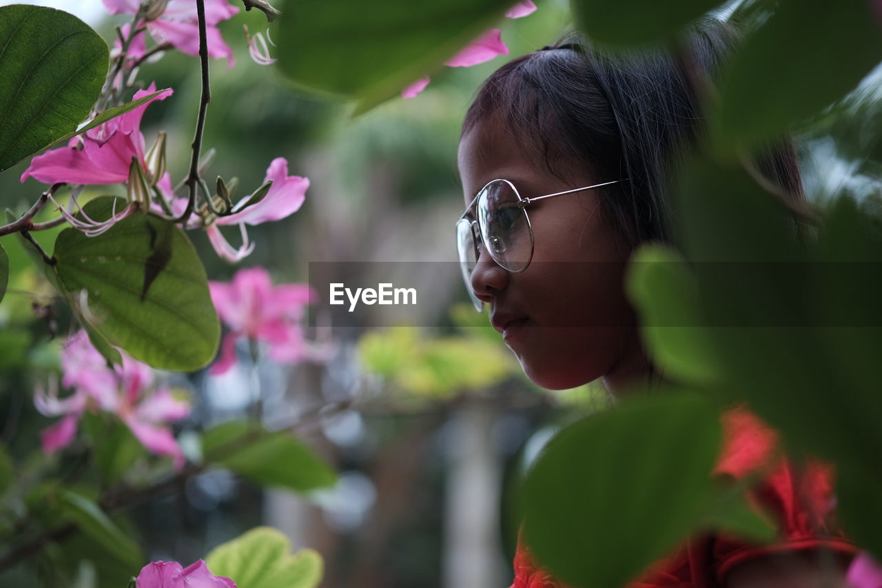 Girl wearing oversized eyeglasses while looking at pink flowering plants in park