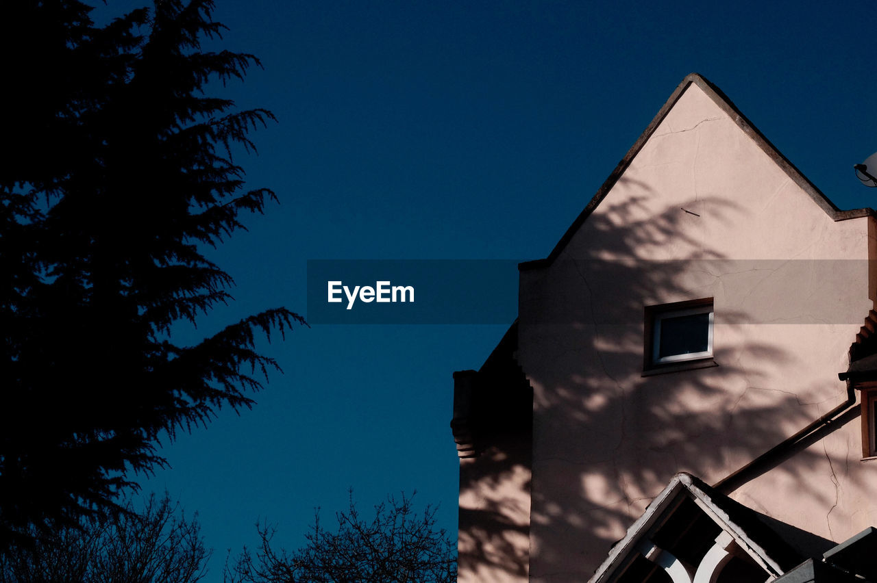 Low angle view of silhouette trees by house during sunny day