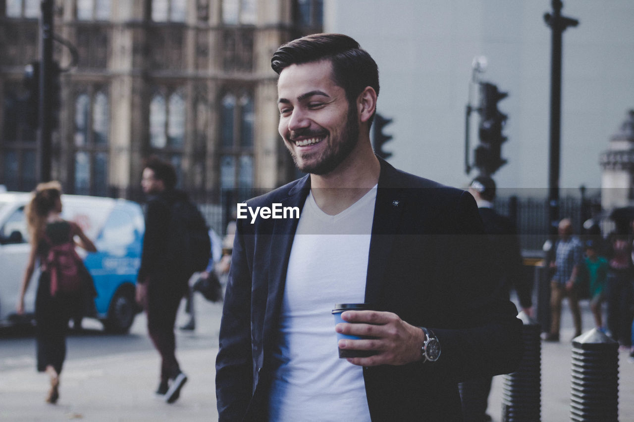 Cheerful businessman holding disposable cup in city