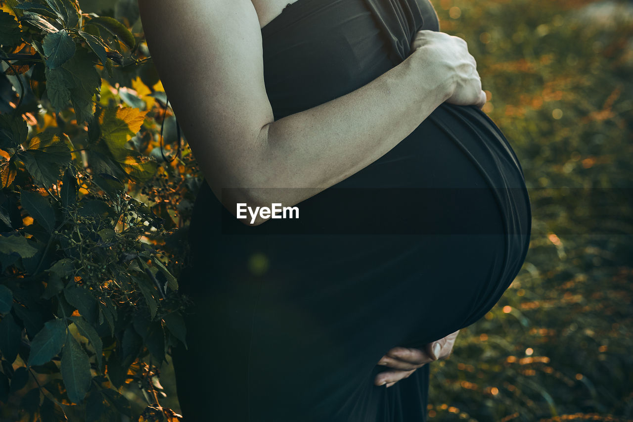 Pregnant woman hugging her tummy standing outdoors surrounded by nature. pregnancy, expectation