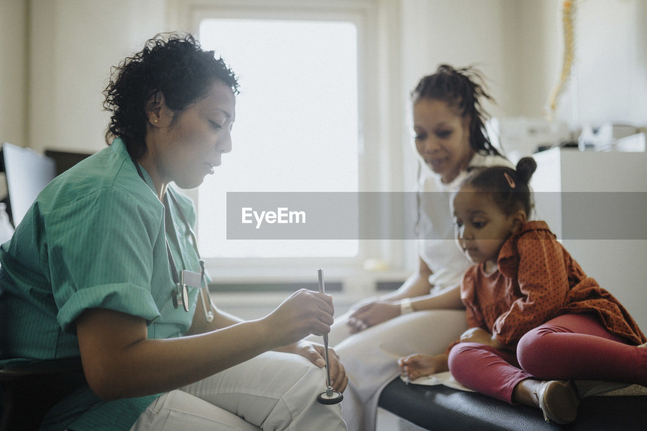 Female pediatric holding reflex hammer discussing with patient in hospital