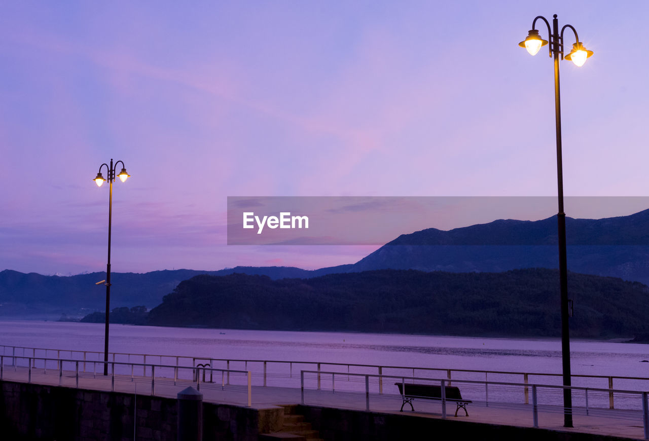 STREET LIGHTS BY MOUNTAINS AGAINST SKY AT SUNSET