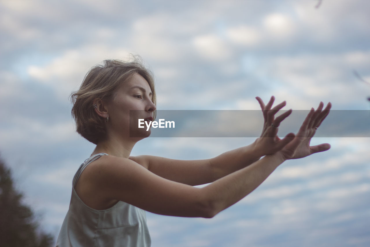 Beautiful woman dancing against cloudy sky