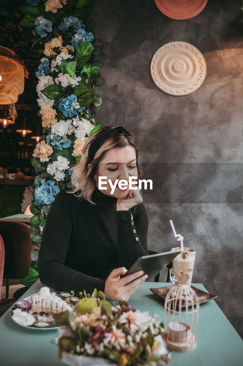 YOUNG WOMAN USING MOBILE PHONE AT TABLE