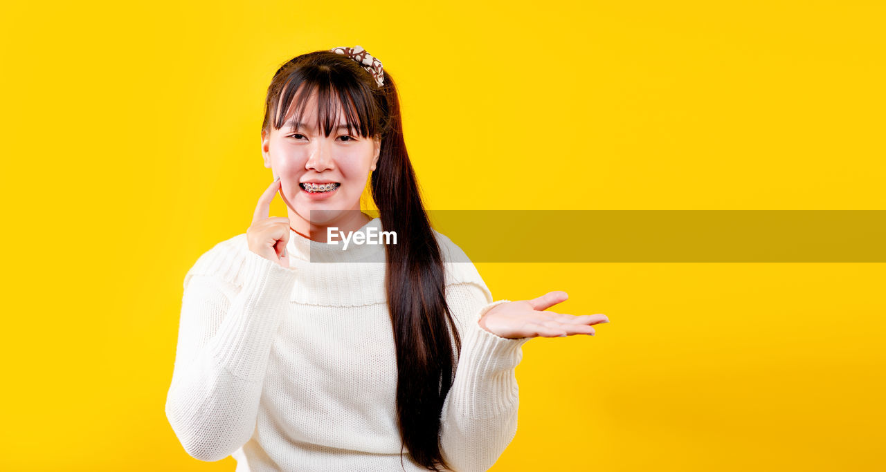 Portrait of smiling young woman against yellow background