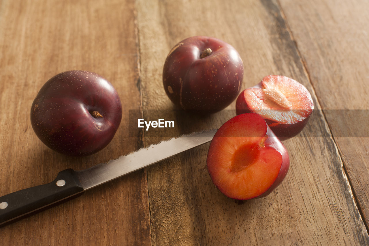 Three whole and cut raw plums with long knife knife on old brown wooden table table