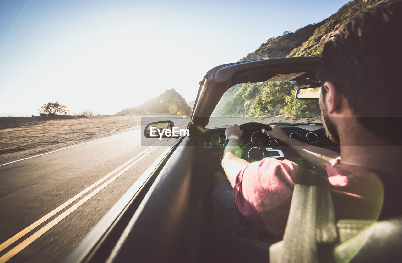 REAR VIEW OF MAN DRIVING CAR ON ROAD