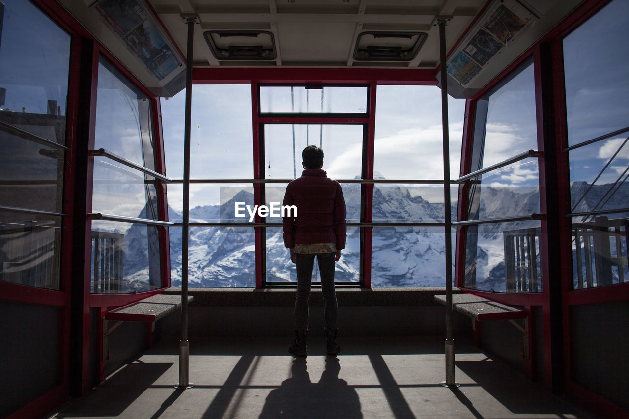 Rear view of person looking towards snowcapped mountains through ski lift windows