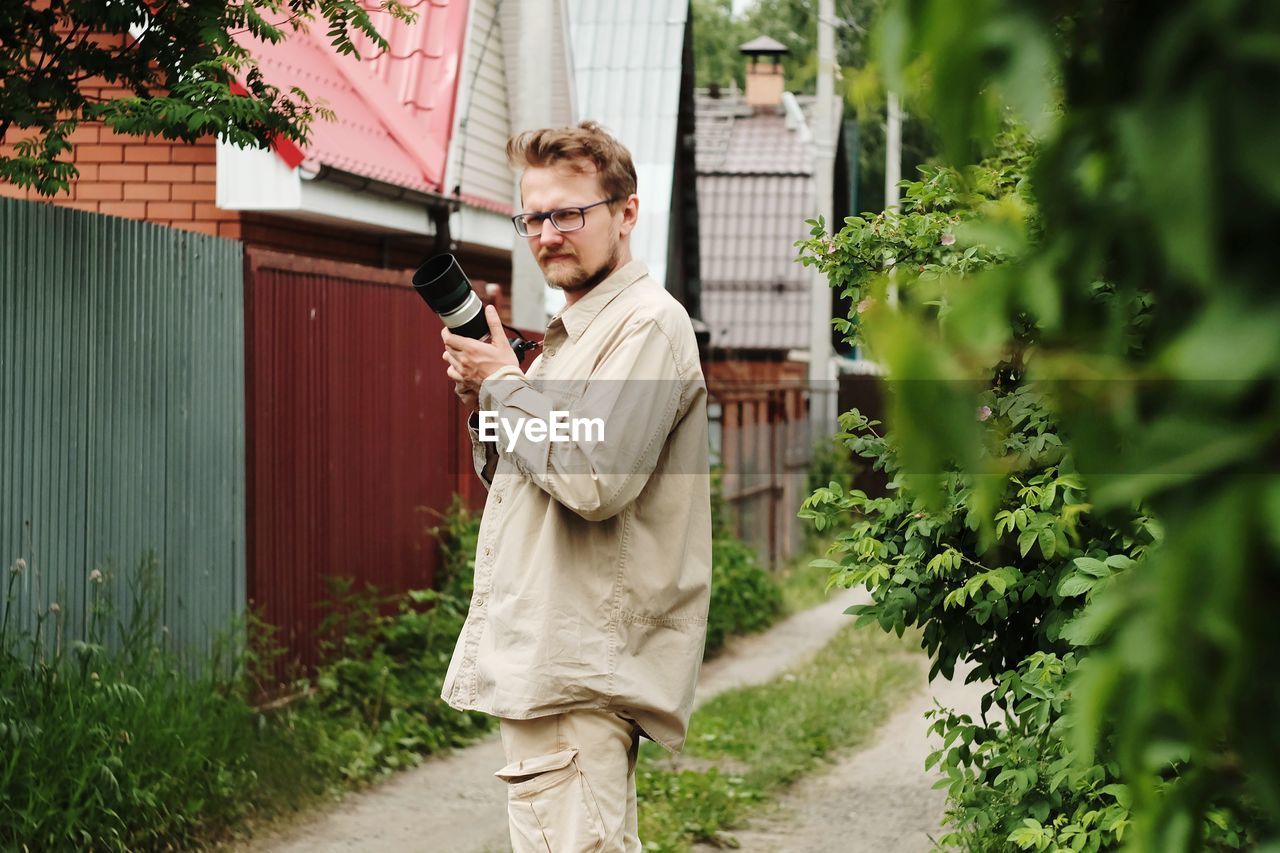 Man with a camera standing against plants in the village