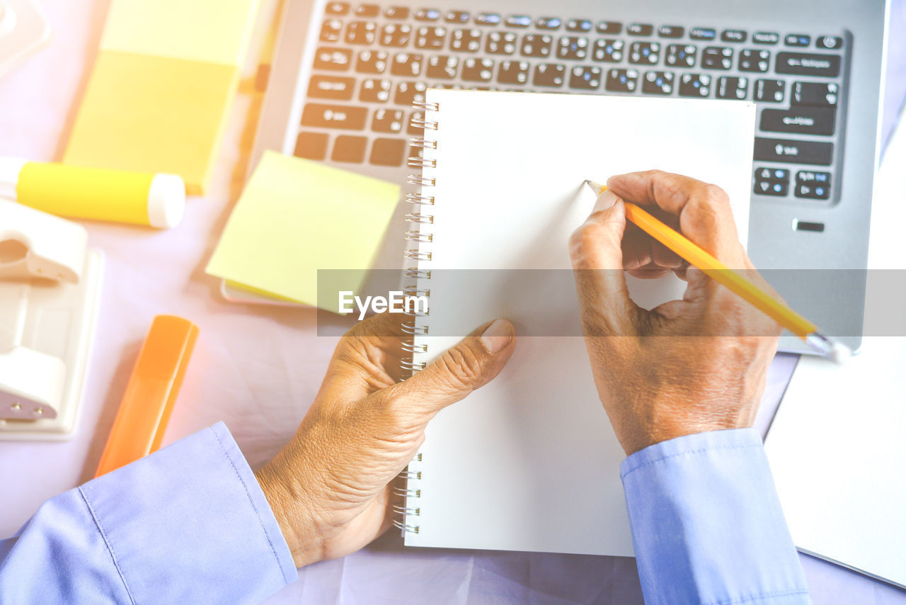 Cropped hands of businessman writing on notepad at desk