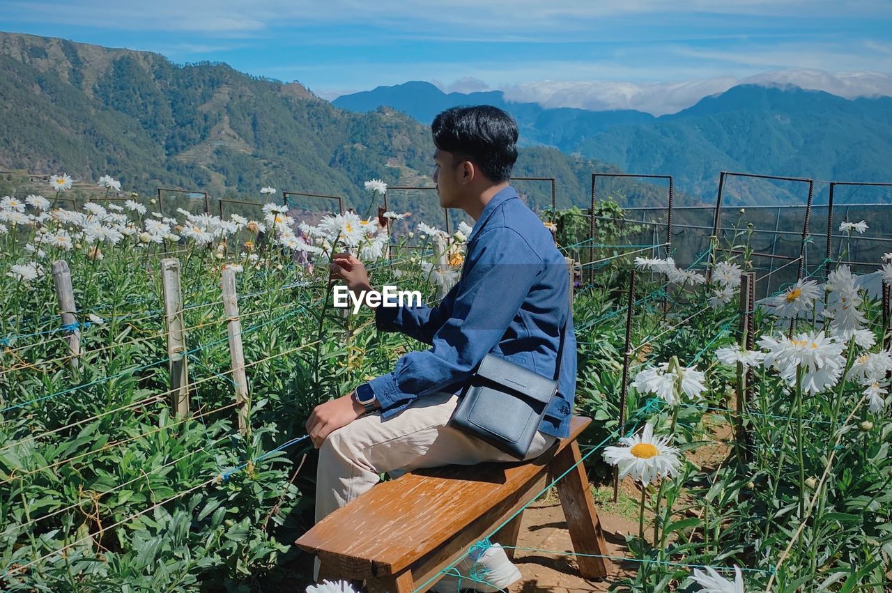 Side view of man sitting on field against mountain