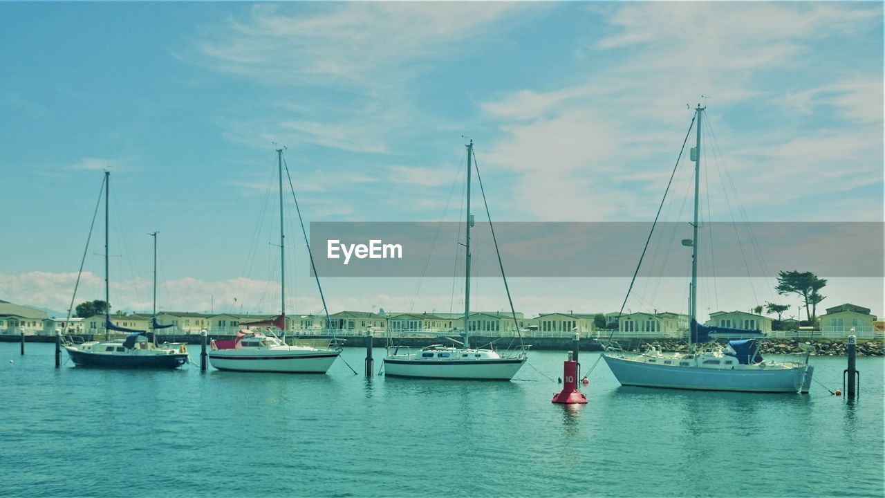 SAILBOATS MOORED ON HARBOR AGAINST SKY