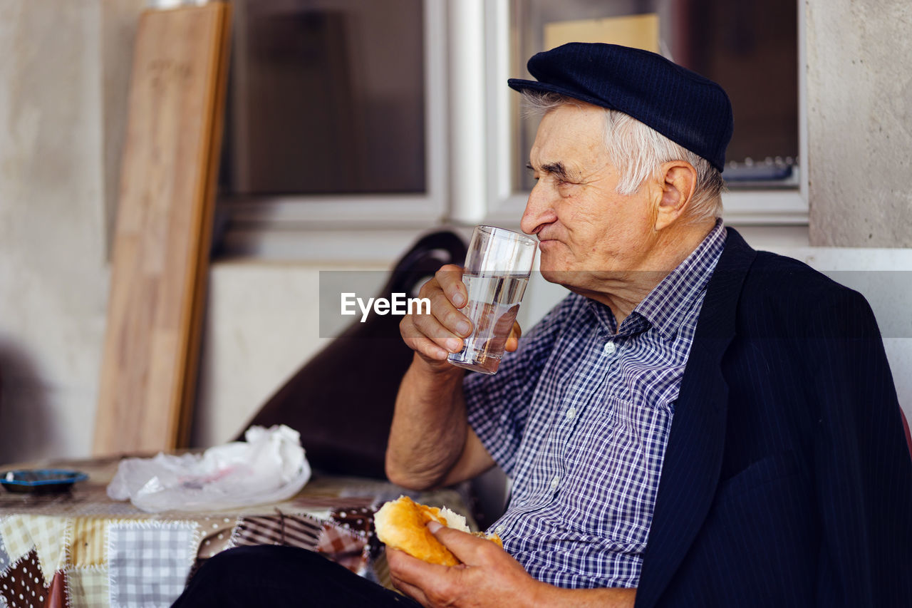 Senior man having food and drink while sitting on seat