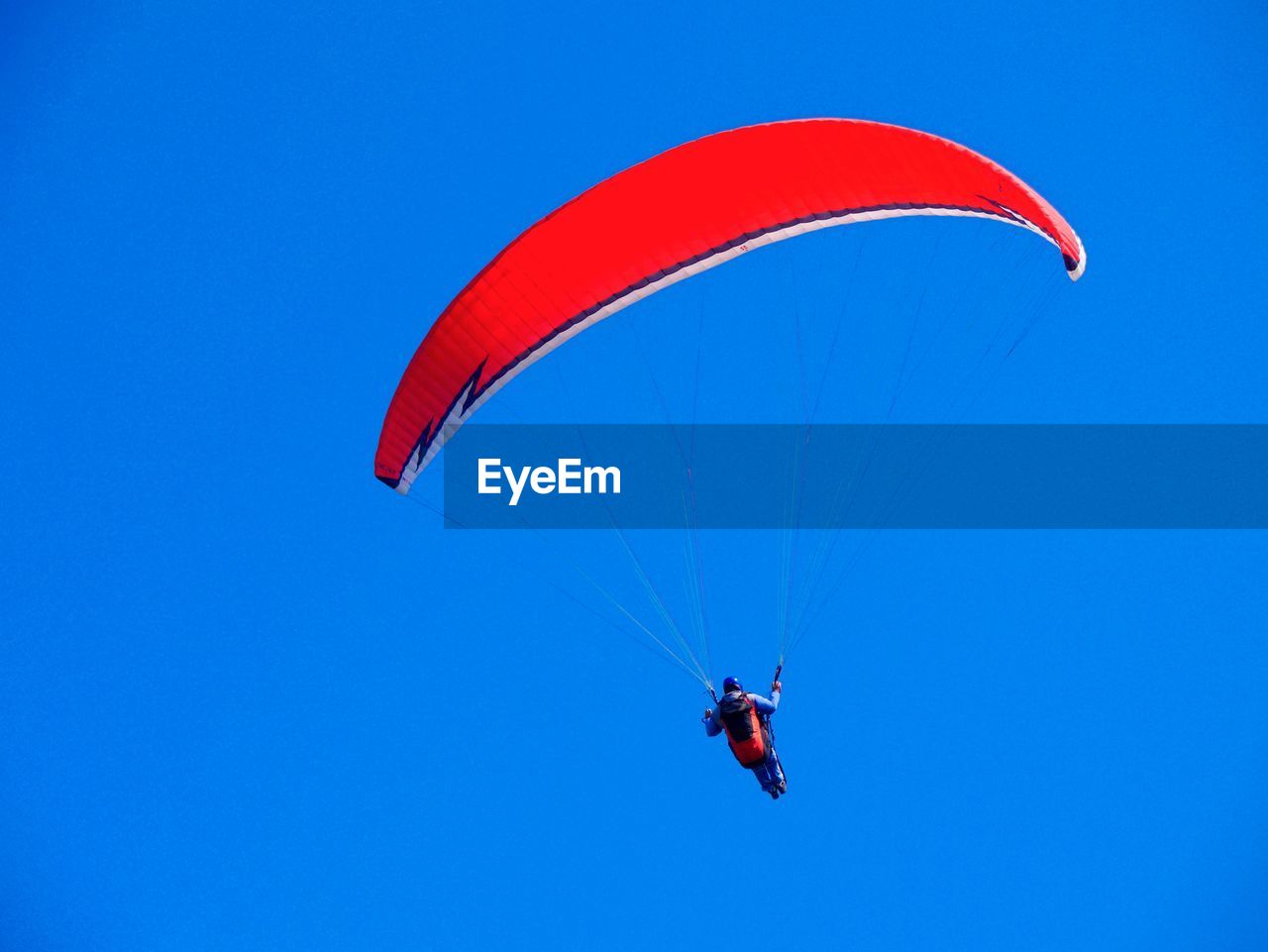 Low angle view of man paragliding against clear blue sky