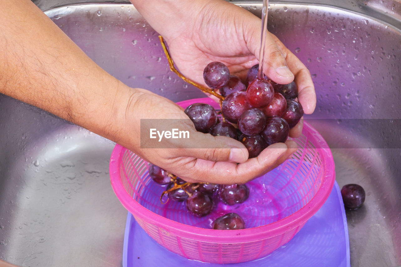 Cropped hands of man cleaning grapes in sink
