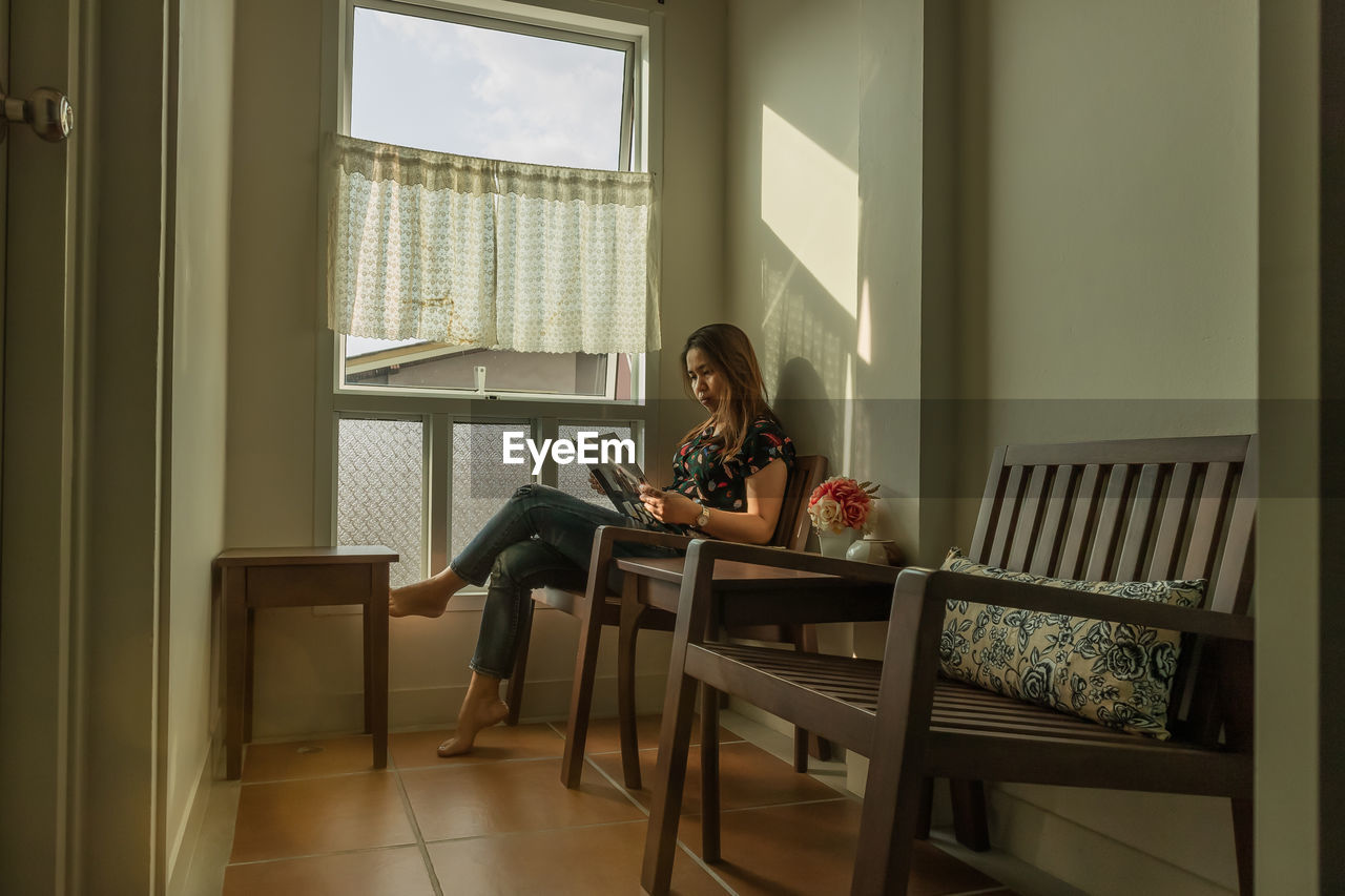 Woman reading book while sitting on chair at home