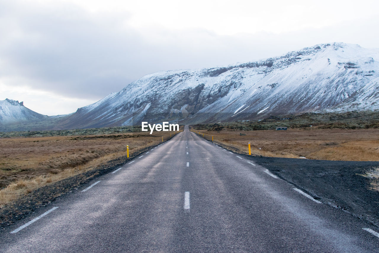 Road leading towards snowcapped mountains against sky