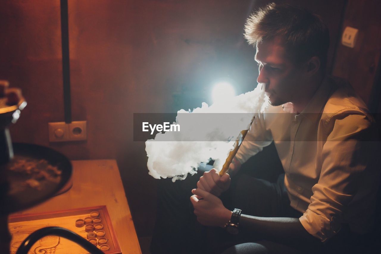 Young man smoking hookah at home