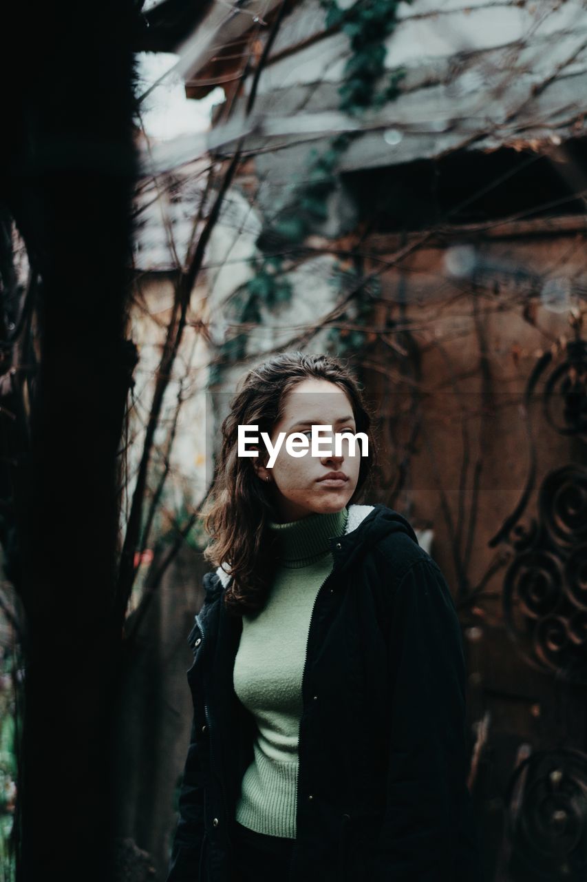 Young woman looking away while standing against tree