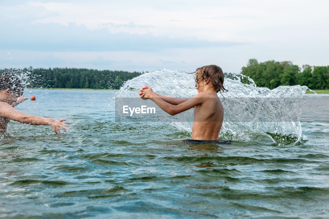 Full length of two boys splashing water in lake against sky