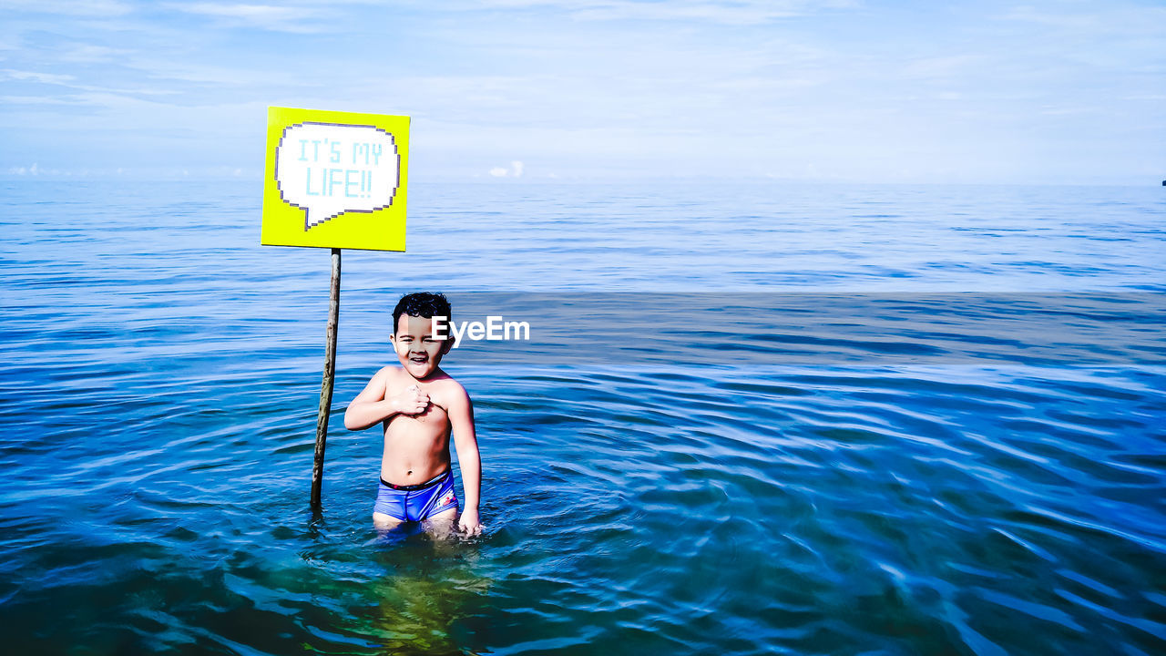 Little shirtless boy standing by sign in sea