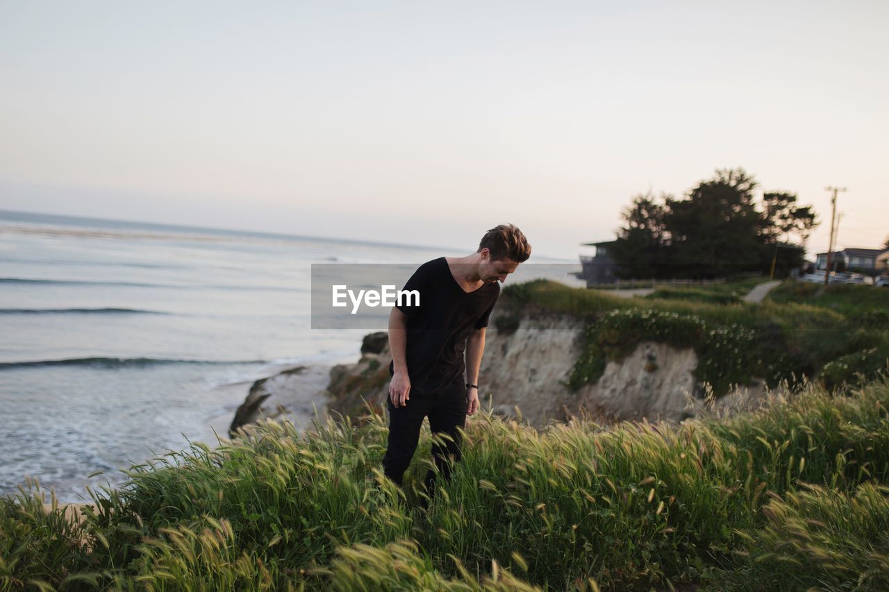 Man standing on mountain by sea against clear sky