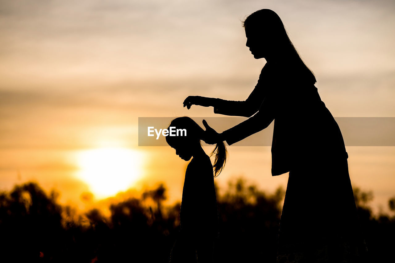 Silhouette of mother and daughter on field at sunset