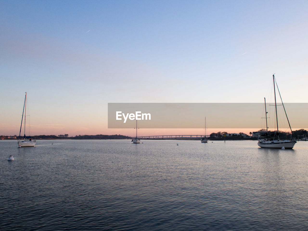 SAILBOATS MOORED IN SEA AGAINST SKY DURING SUNSET