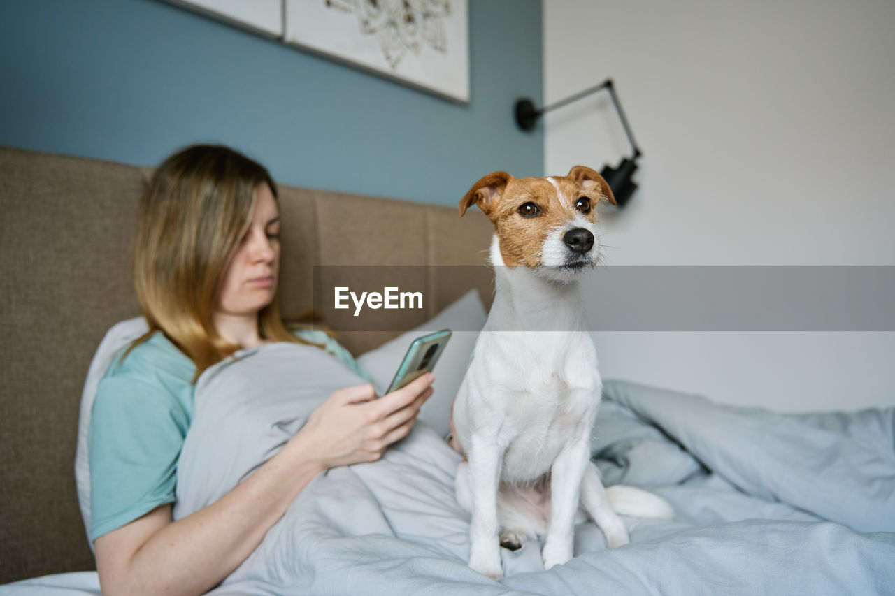 Woman with dog chilling on bed, use smartphone