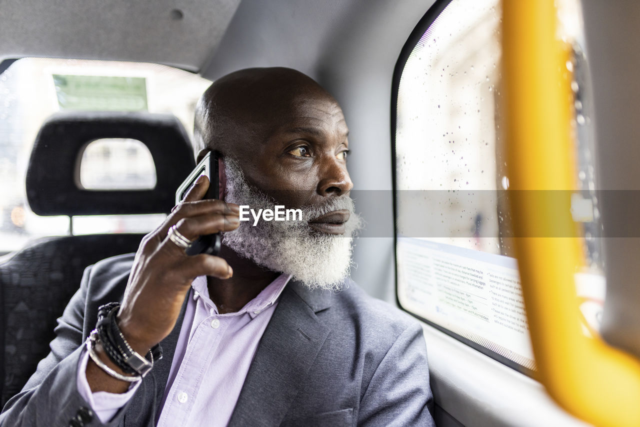 Senior businessman talking on smart phone and looking through window in taxi