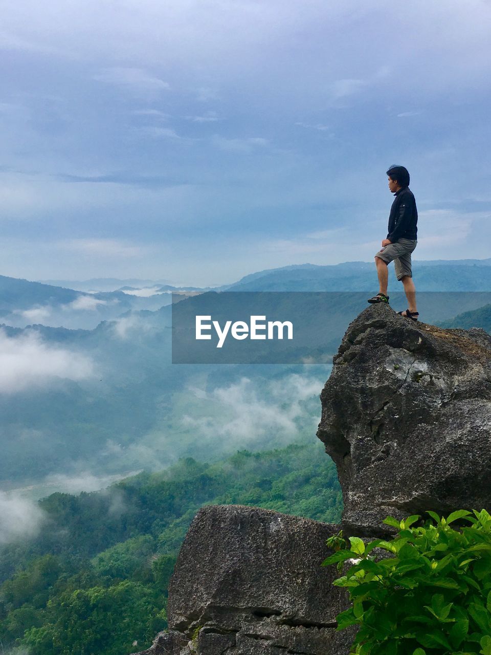 Full length of man standing on cliff against mountains and sky