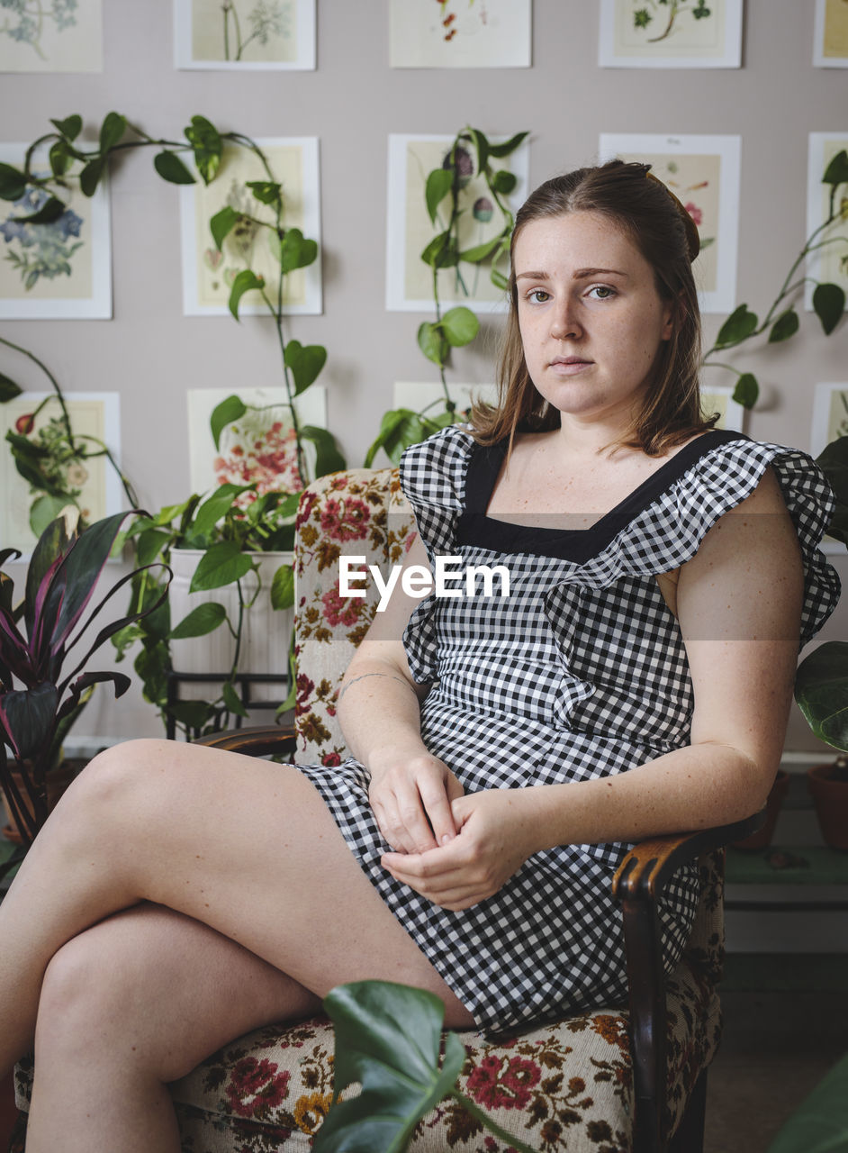 Stylish young woman sits in chair in front of plants and art