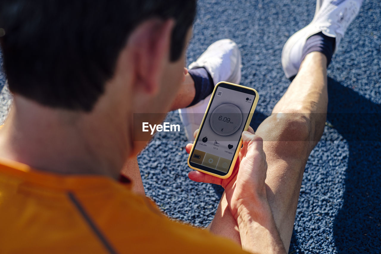 Sportsman holding mobile phone sitting on track