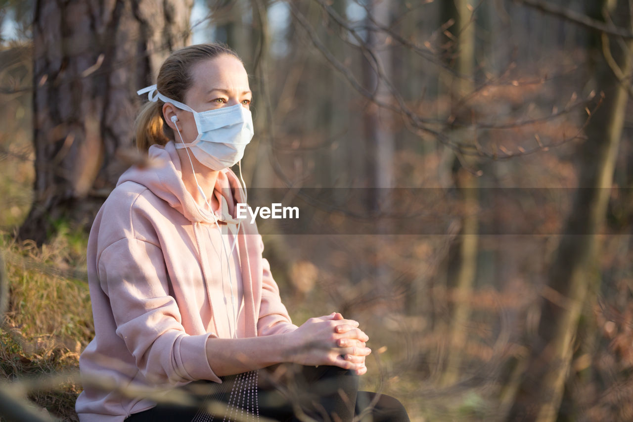 Woman wearing mask sitting in forest