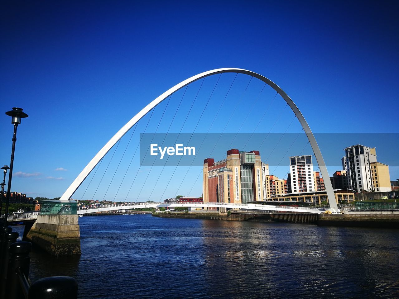 Bridge over river by city against clear blue sky