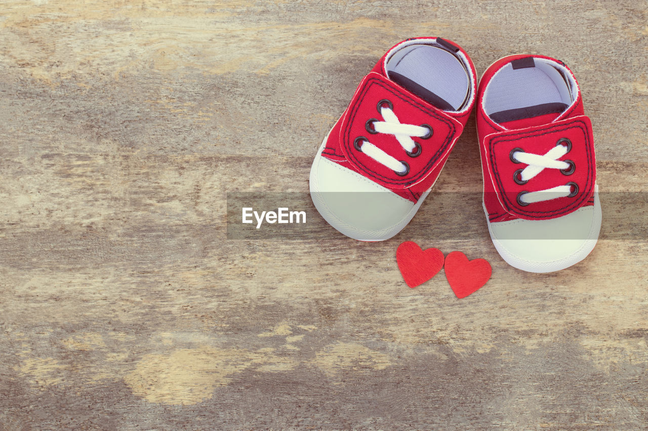 Directly above shot of baby shoes and heart shapes on wooden table