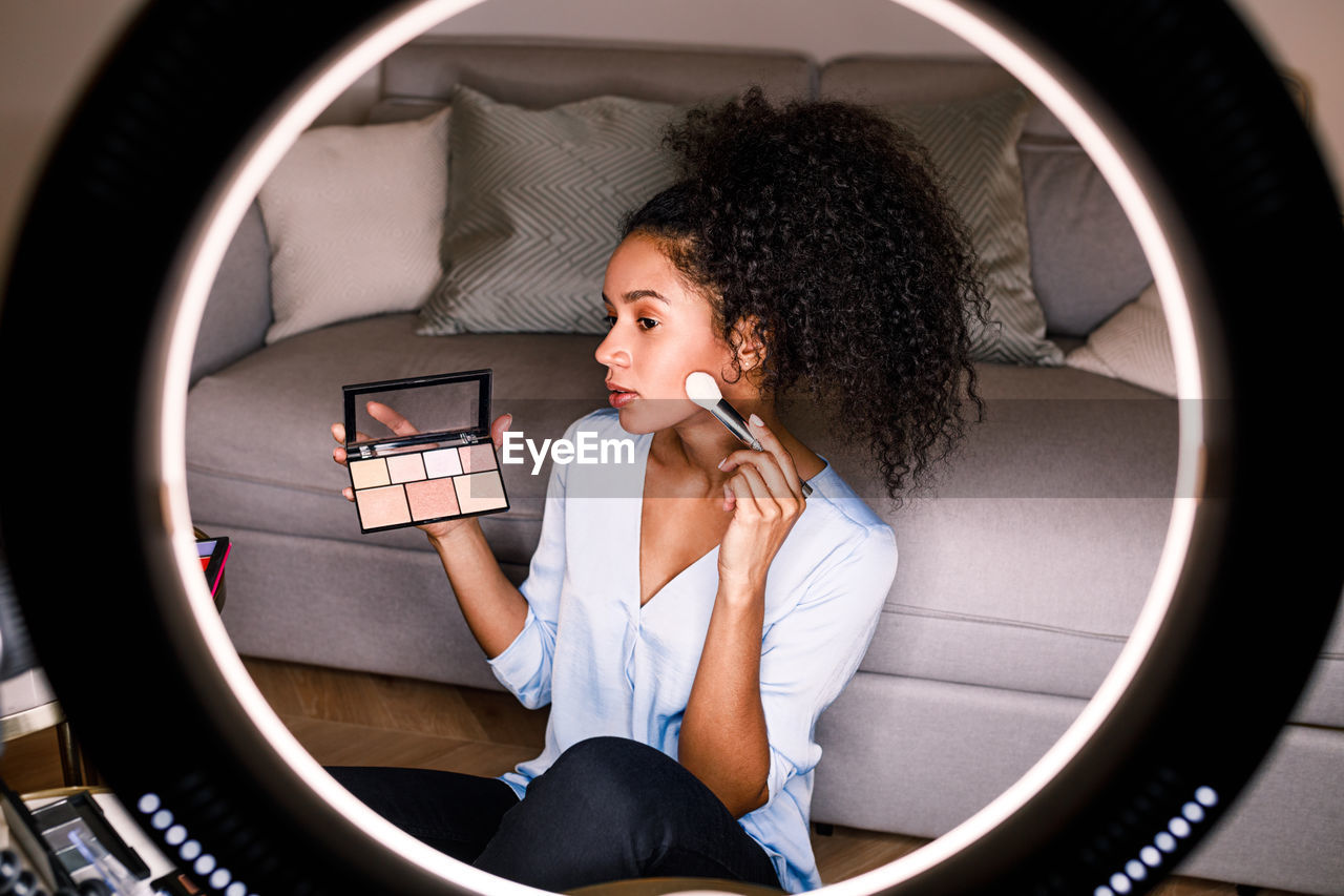 Woman applying face powder seen through lens at home