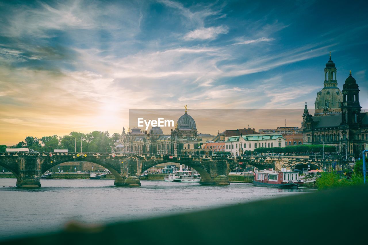 Arch bridge over river amidst buildings against sky in city