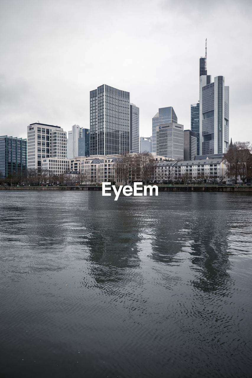 BUILDINGS BY RIVER AGAINST SKY IN CITY