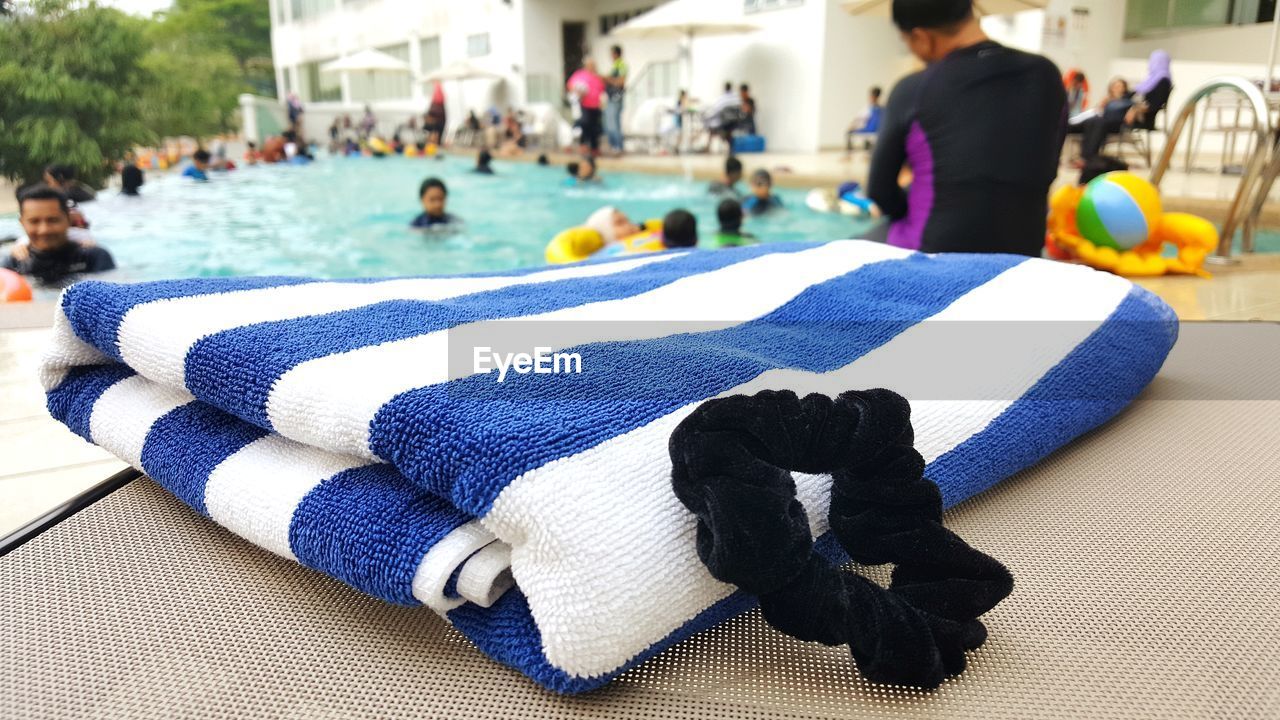 Close-up of towel and hair elastic against people in swimming pool